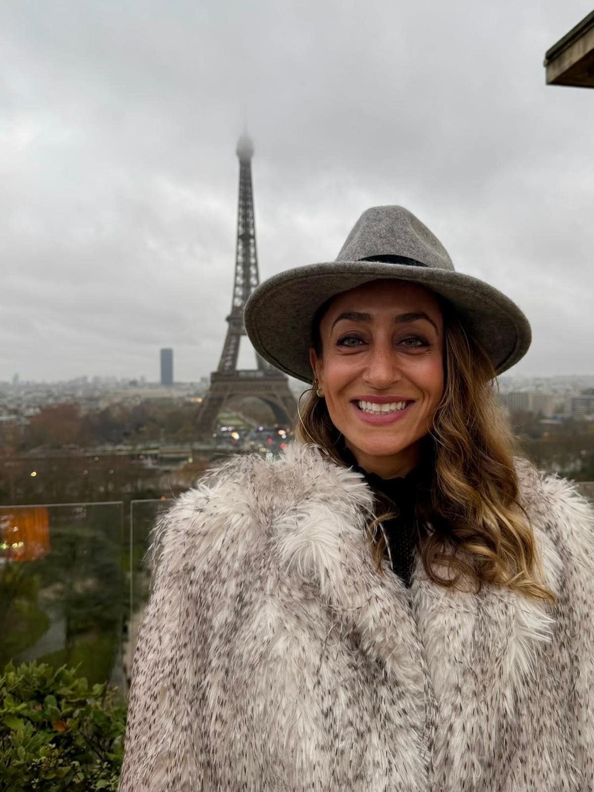 Smiling woman with hat and fur coat in Paris with Eiffel Tower in background.