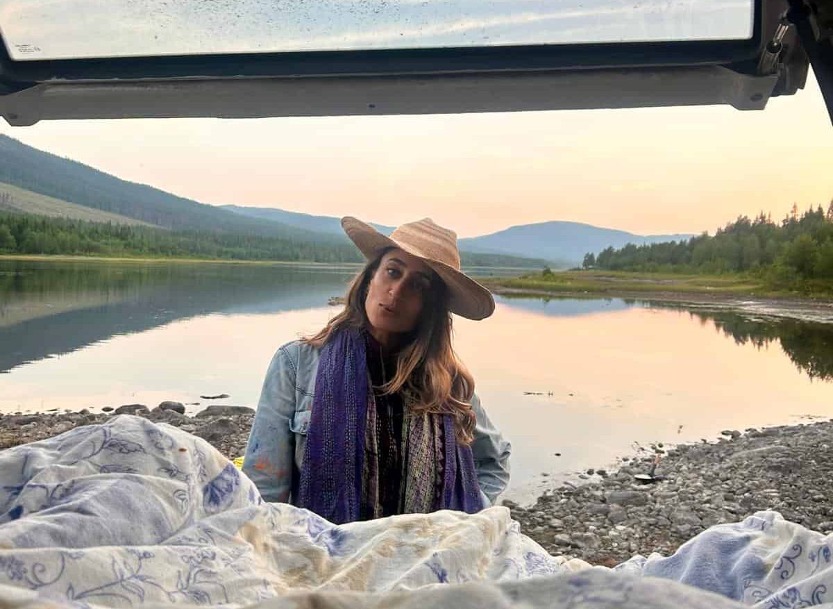 Woman in a hat enjoying a peaceful river view at sunset.